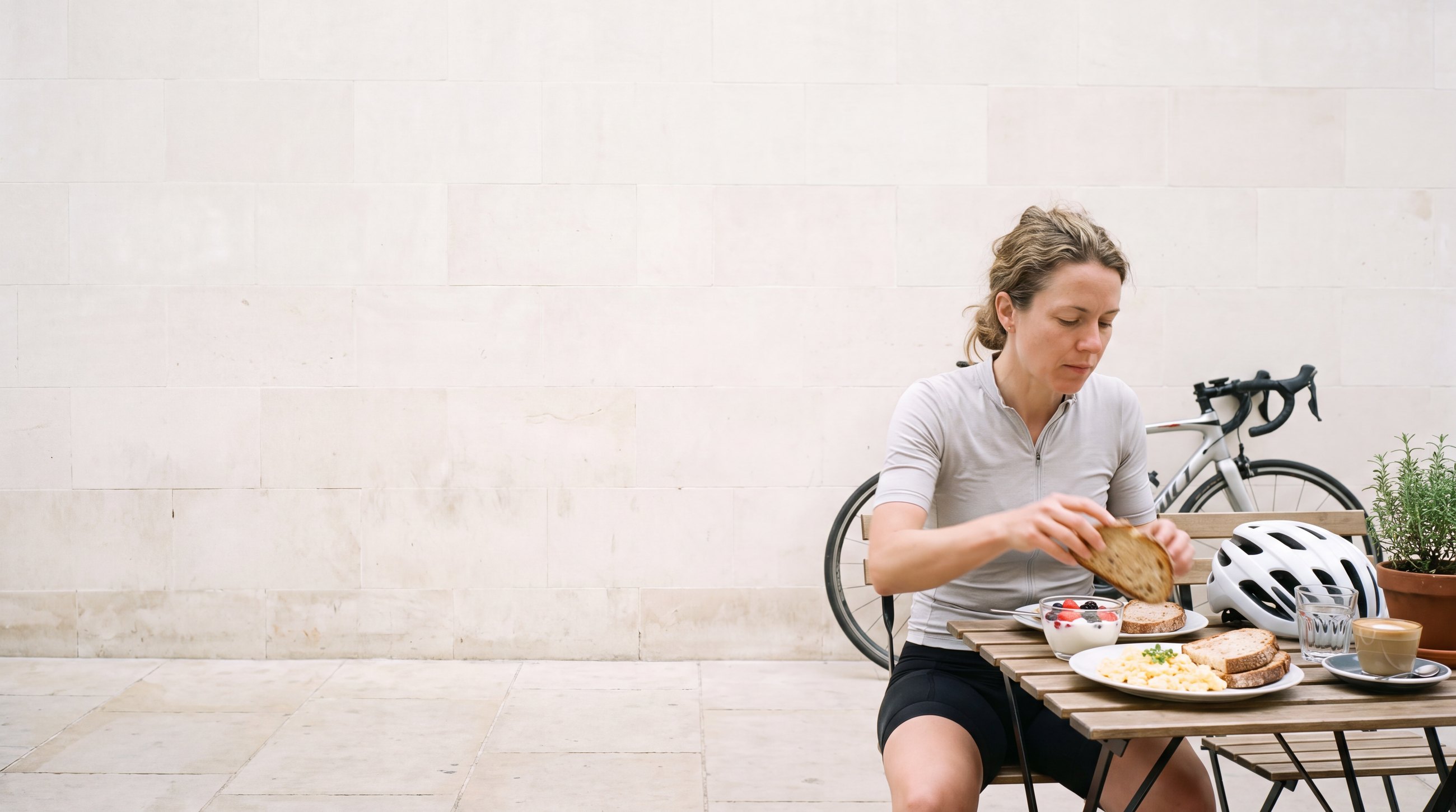 A road cyclist sitting at a café table after a ride, helmet off on the table, eating eggs, sourdough and yoghurt with berries.